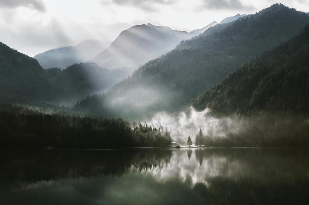morning sun breaking through the clouds over a forested mountain lake